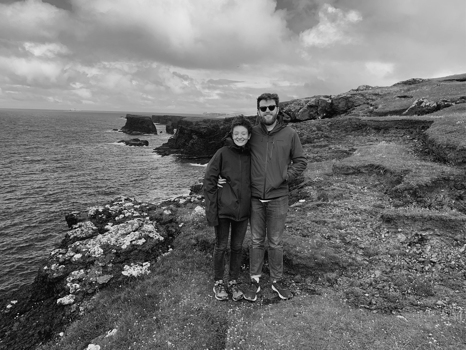 Jack and Sarah stood at the edge of a cliff in Shetland, smiling for the camera